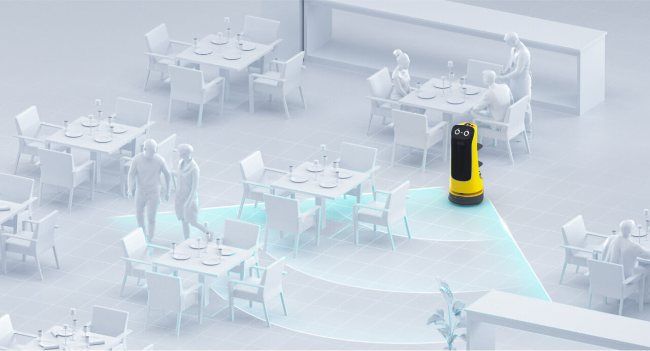 Kerfuś ma następcę. To robot KettyBot Pro. Restauracja z białymi meblami i postaciami ludzkimi, w centrum robot do obsługi w kolorze żółto-czarnym.