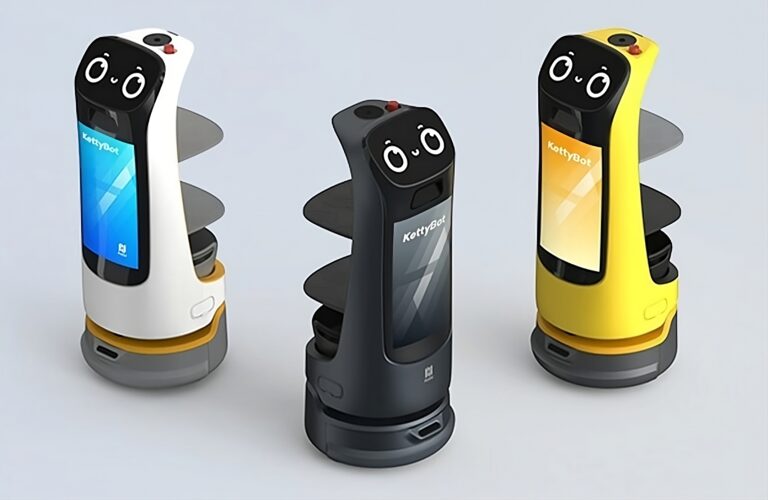 Trzy kolorowe roboty KettyBot Pro z oczami na wyświetlaczach na białym tle, od lewej w kolorach biało-złotym, czarnym i żółto-czarnym.