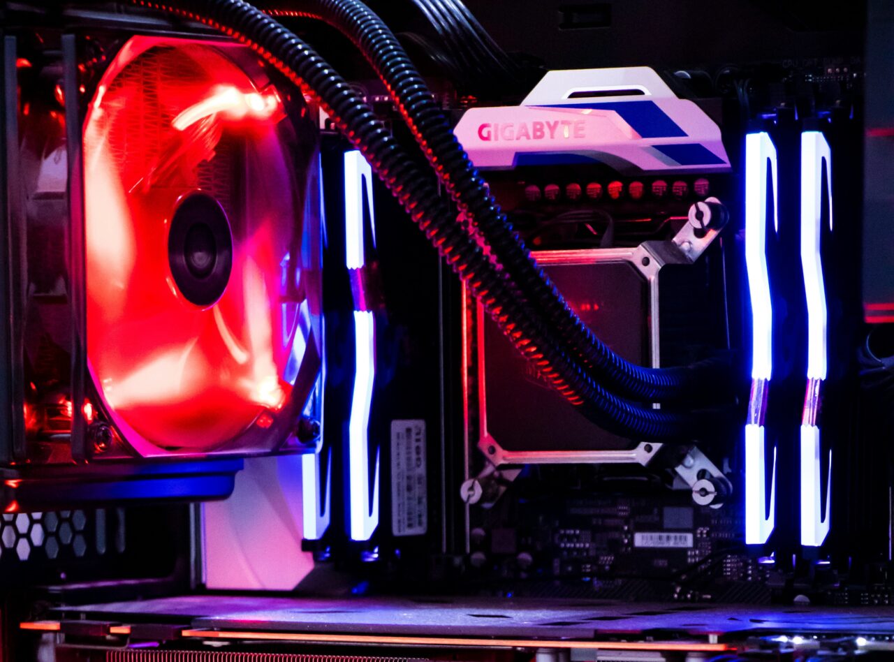 Wnętrze komputera PC z podświetleniem LED, w tym czerwone oświetlenie wentylatora chłodzenia i niebieskie paski świetlne wokół pamięci RAM oraz na płycie głównej z logo GIGABYTE.