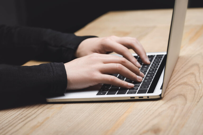 Osoba pisząca na klawiaturze laptopa ustawionego na drewnianym biurku.