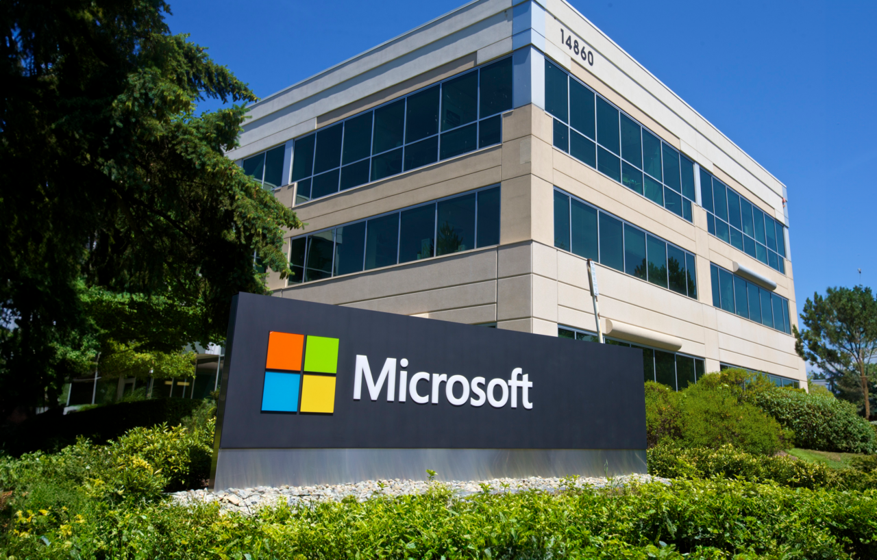Tablica z logo firmy Microsoft organizującej microsoft build przed budynkiem biurowym otoczonym zielenią.