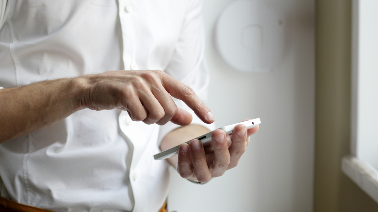 Cyberflasher z Anglii. Osoba w białej koszuli używa smartfona, dotykając palcem ekranu.