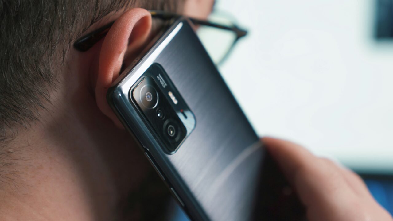 Osoba trzymająca smartfon przy uchu, skupienie na aparacie fotograficznym telefonu.