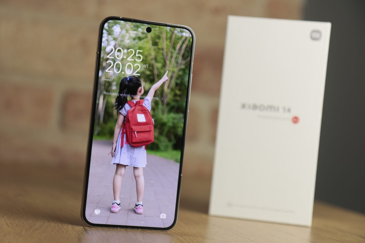 Smartfon Xiaomi z wyświetlaczem pokazującym zdjęcie dziewczynki z plecakiem oraz opakowanie z napisem "Xiaomi 14".