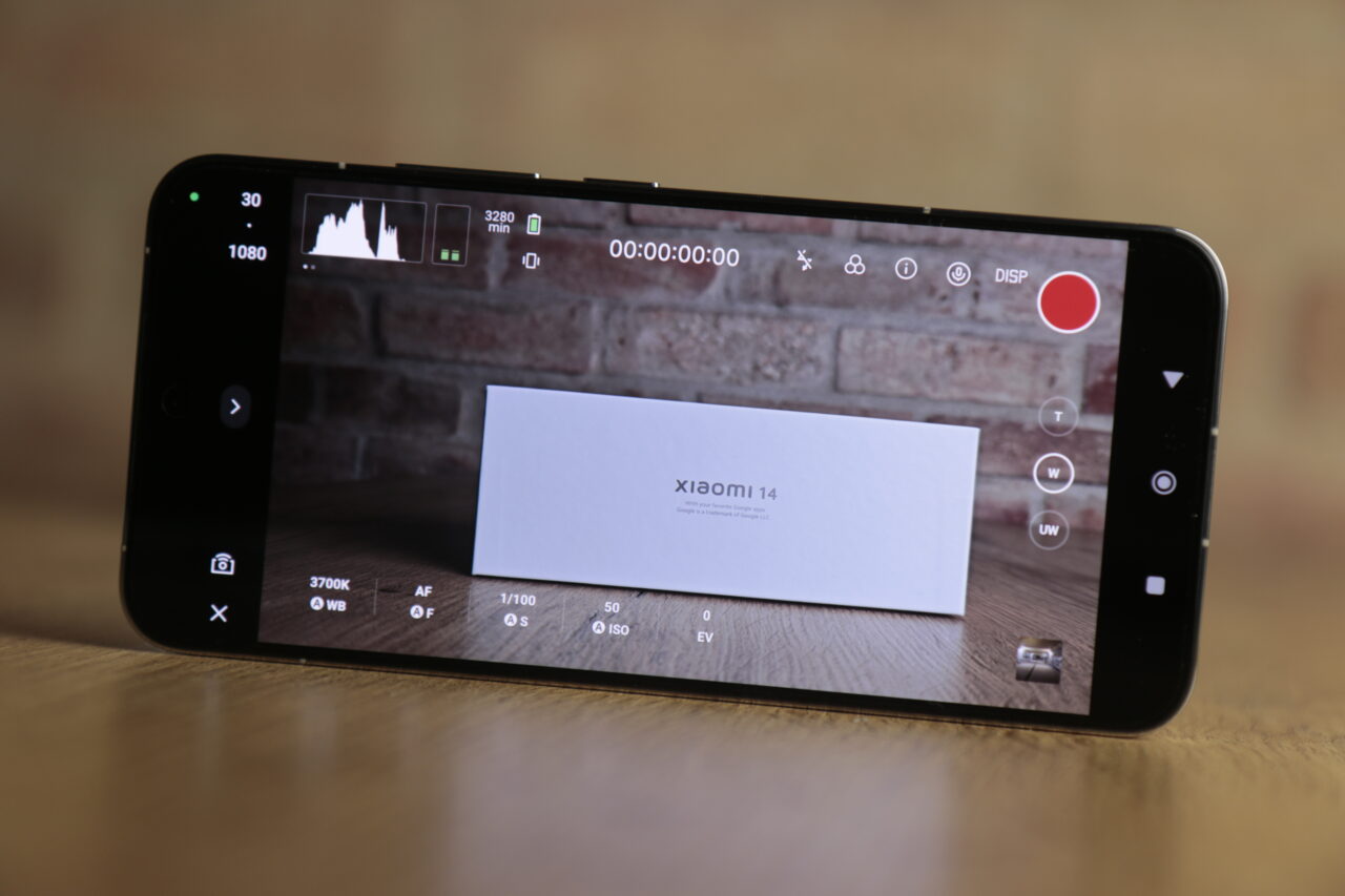 Smartfon leżący na drewnianym blacie, wyświetlający widok białej wizytówki z napisem "xiaomi 14" na ekranie aparatu, z włączonym interfejsem użytkownika aparatu fotograficznego.