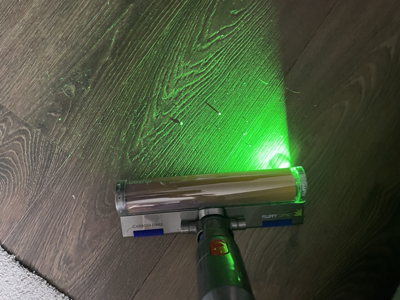 Odkurzacz bezprzewodowy z lampą UV podświetlającą kurz na ciemnym drewnianym podłogowym.