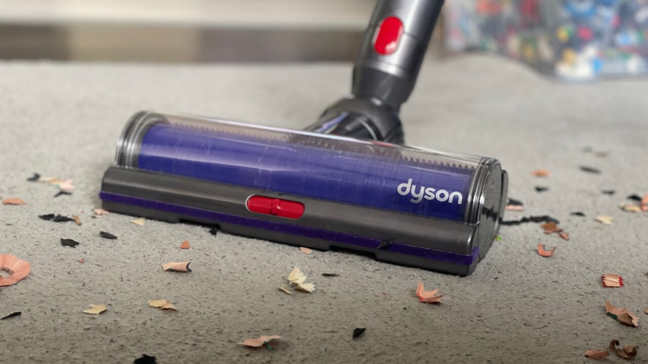 Odkurzacz bezprzewodowy marki Dyson na dywanie, zbierający okruchy i śmieci.
