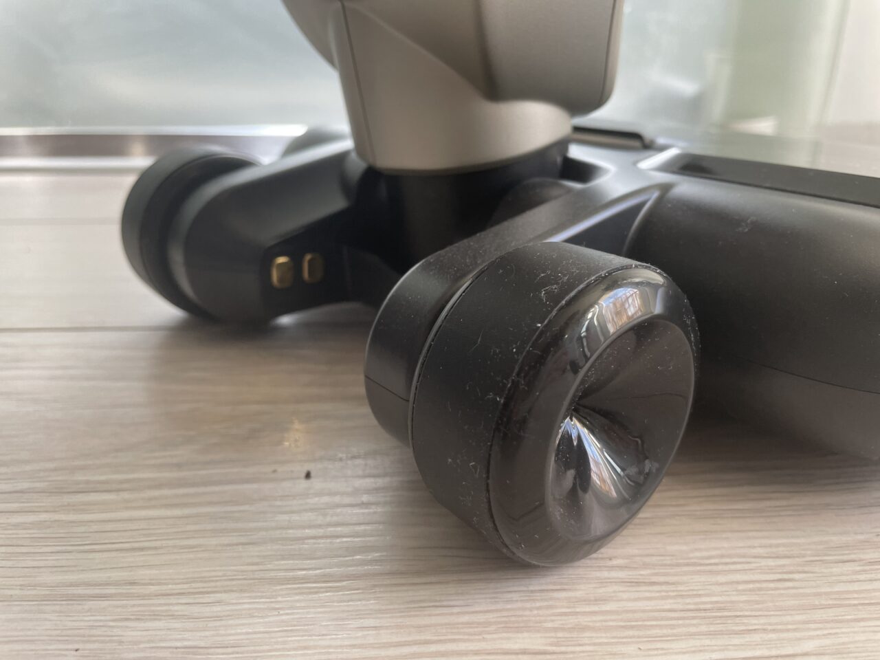 Czarny, przenośny głośnik Bluetooth leżący na drewnianym blacie, z widocznymi zakurzonymi kółkami i złączami do ładowania.