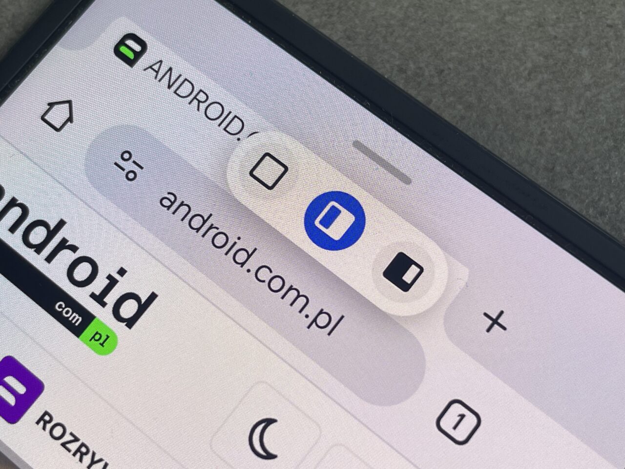 Zbliżenie na ekran smartfona z otwartą przeglądarką internetową pokazującą pasek adresu z adresem "android.com.pl" i kilka ikon interfejsu użytkownika.