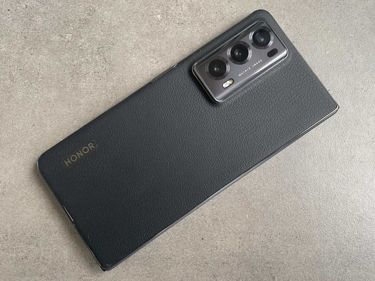 Czarny smartfon marki Honor z pokrowcem i widocznym modułem trzech aparatów fotograficznych na szarym tle.