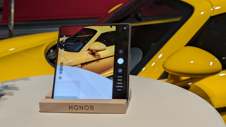 Smartfon Honor umieszczony na stojaku z odbiciem żółtego samochodu w jego ekranie.