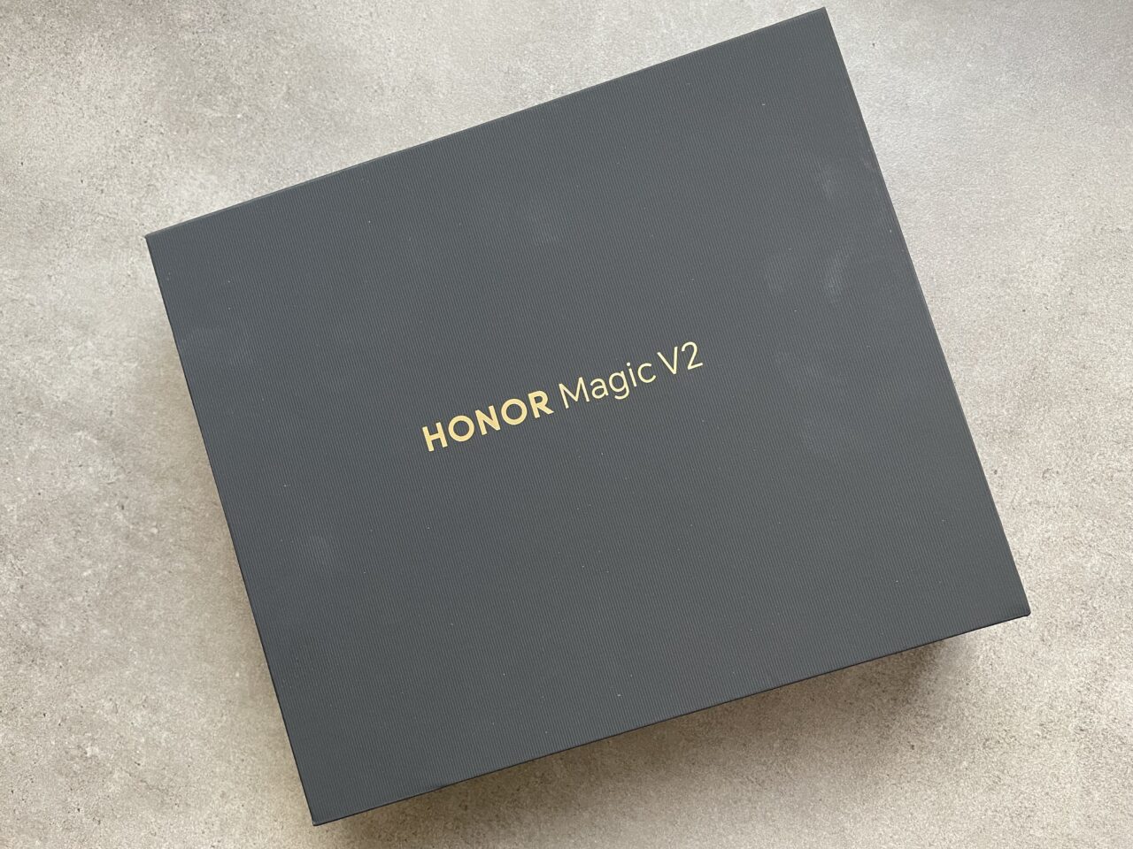 Czarne pudełko z napisem "HONOR Magic V2" umieszczone na szarej powierzchni.