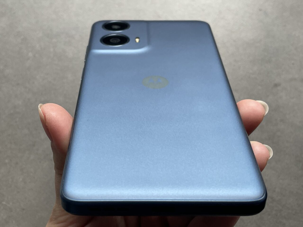 Tylny widok niebieskiego smartfona trzymanego w dłoni z widocznym logo producenta i podwójnym aparatem fotograficznym.