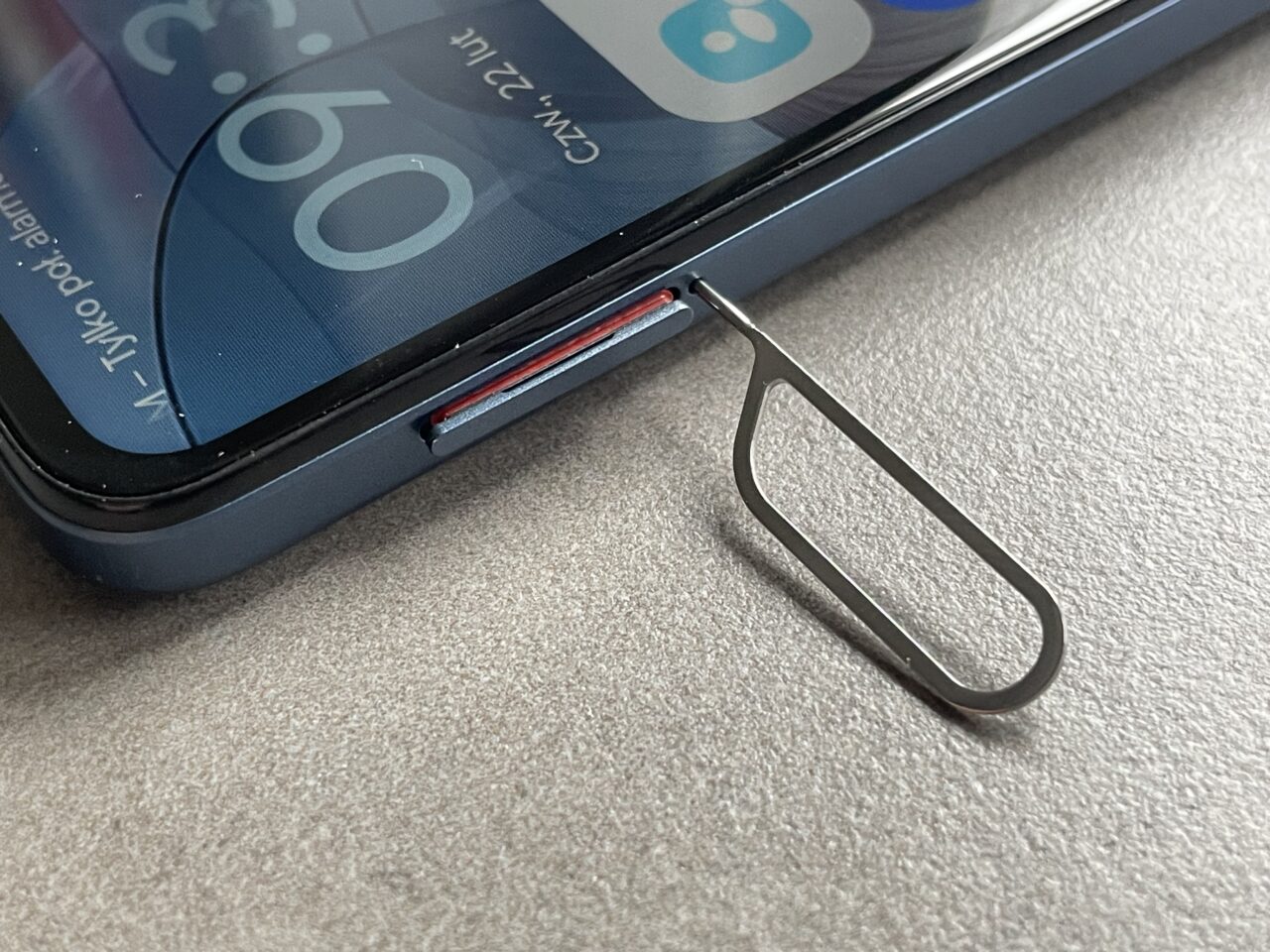 Wyjmowacz karty SIM leży obok zamkniętej szufladki na kartę SIM w smartfonie, który znajduje się na szarym blacie.
