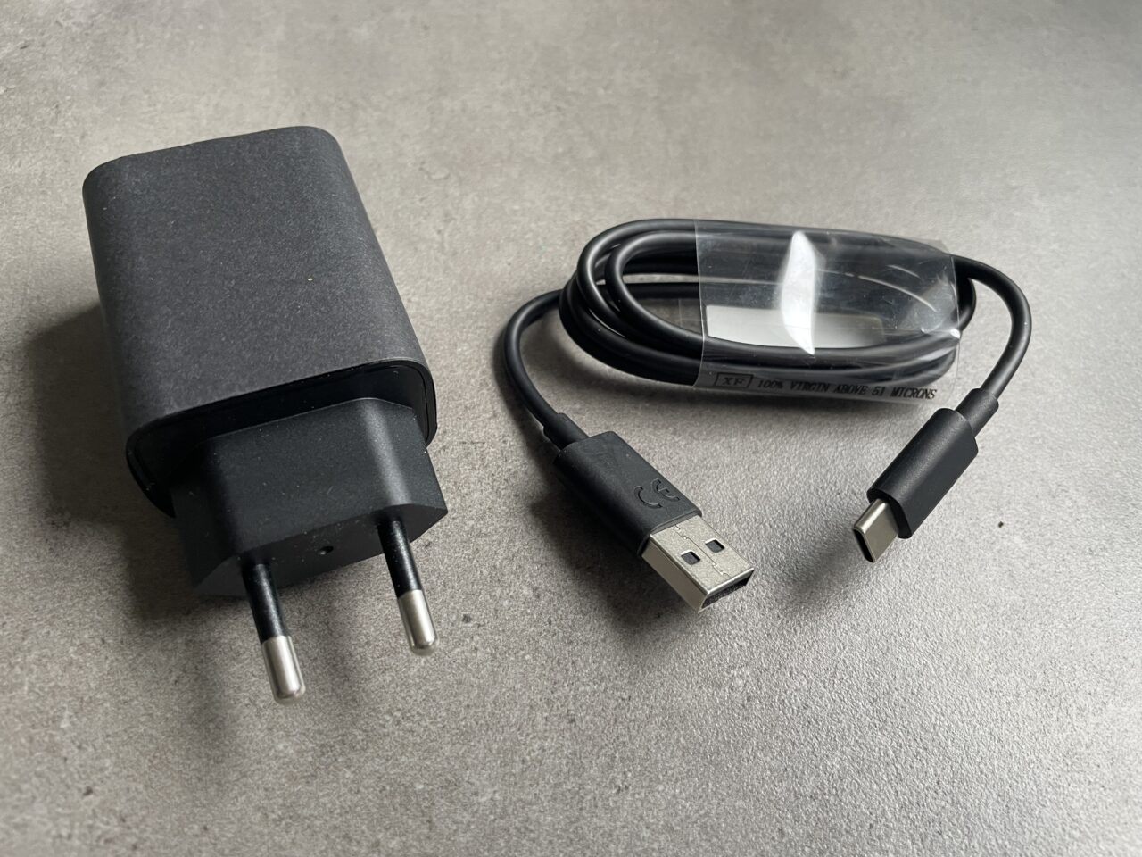 Czarny zasilacz sieciowy i przewód USB-C na szarym tle.