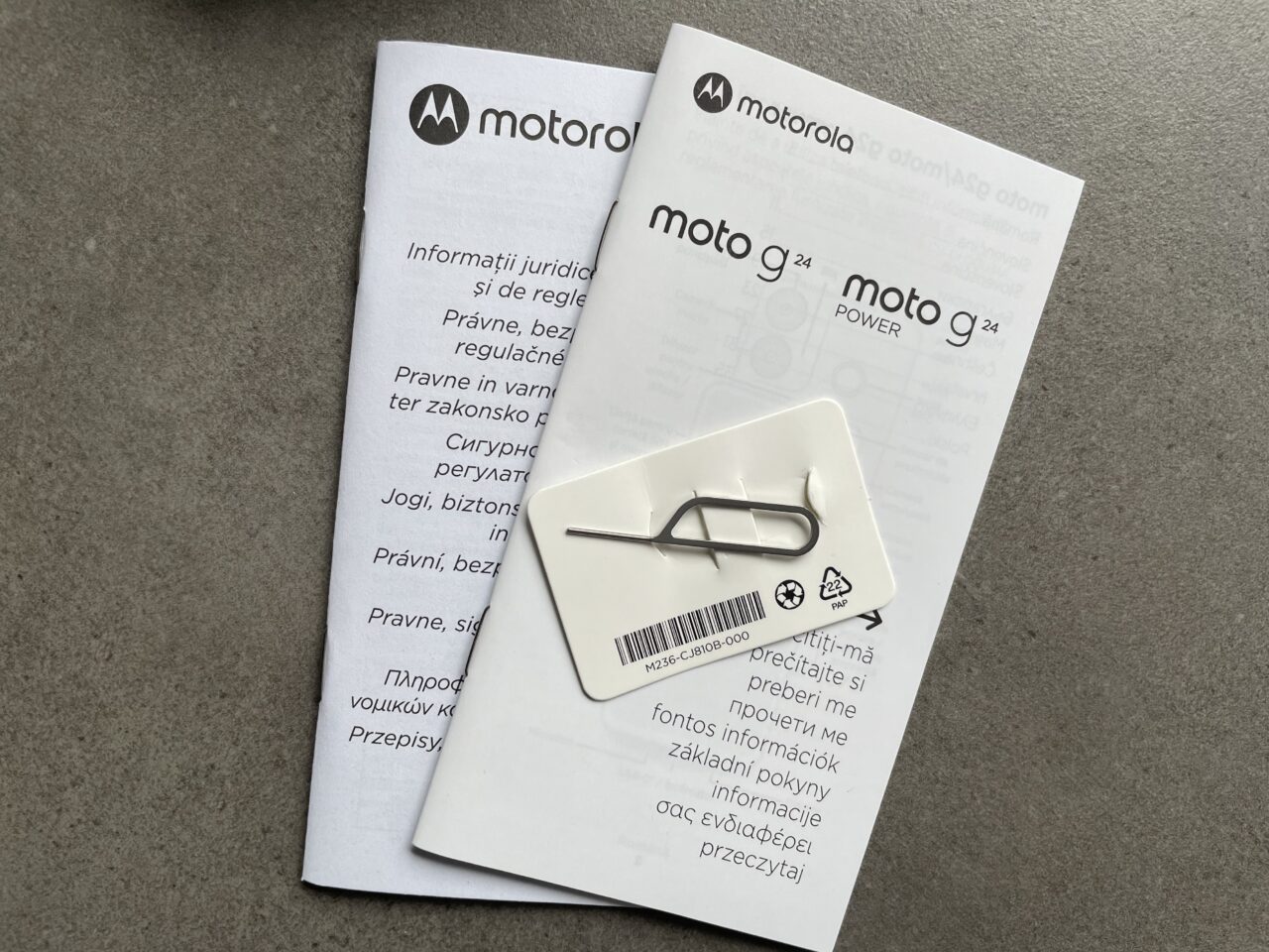 Książeczki z informacjami prawnych marki Motorola i karta SIM z narzędziem do wyjmowania tacki SIM leżą na szarym tle.