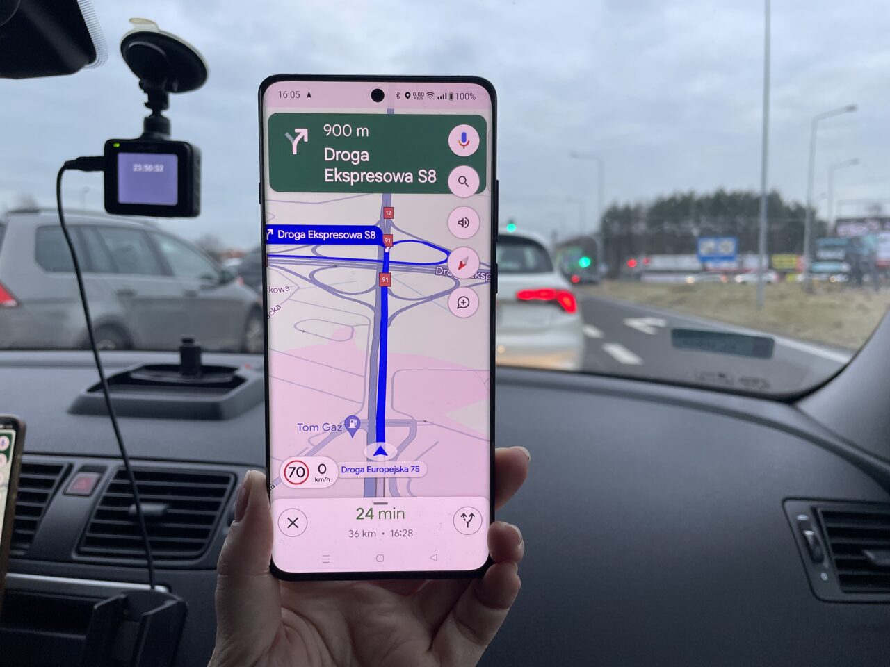Ręka trzymająca smartfon z włączoną aplikacją nawigacyjną pokazującą trasę na drodze ekspresowej S8, w tle widoczna rozmyta sceneria drogi i inne pojazdy.