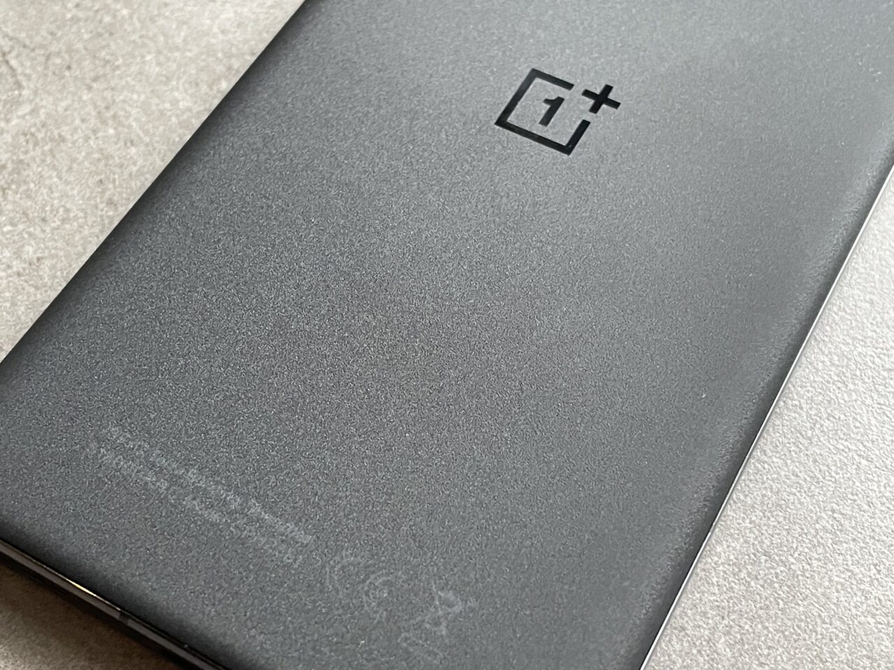 Tylna obudowa smartfona z logo OnePlus na szarym tle.