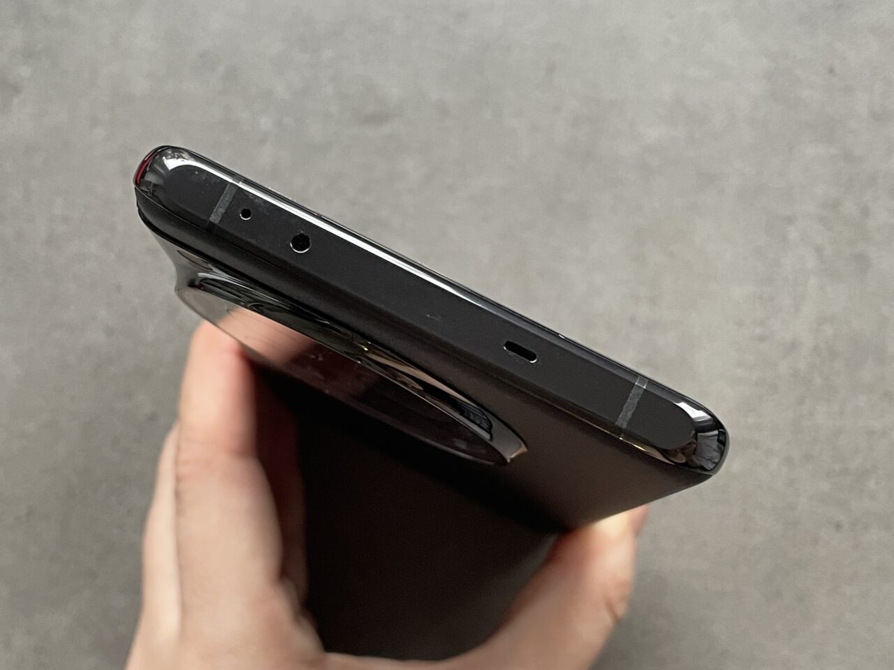 Czarny smartfon trzymany w dłoni z widocznym górnym brzegiem aparatu, pokazując gniazdo słuchawkowe i mikrofon.