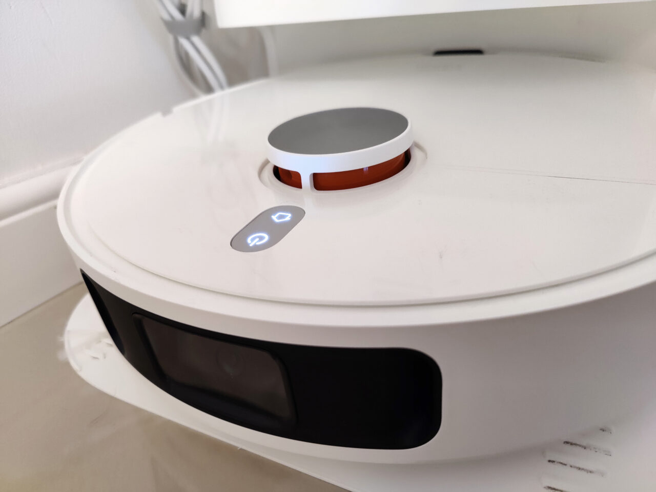 O robô de limpeza branco fica no chão, com botões e um sensor visíveis.