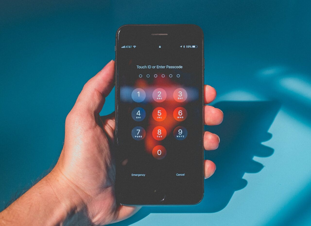 Telefon komórkowy trzymany w dłoni z wyświetlonym ekranem blokady, na którym widać klawiaturę numeryczną do wprowadzenia kodu dostępu.