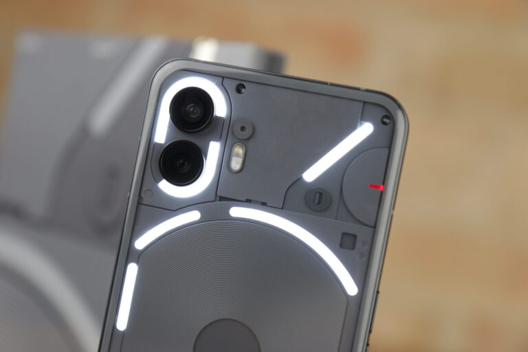 Tylna część czarnego smartfona Nothing Phone 2 ze świecącymi elementami. W tle rozmazane cegły.