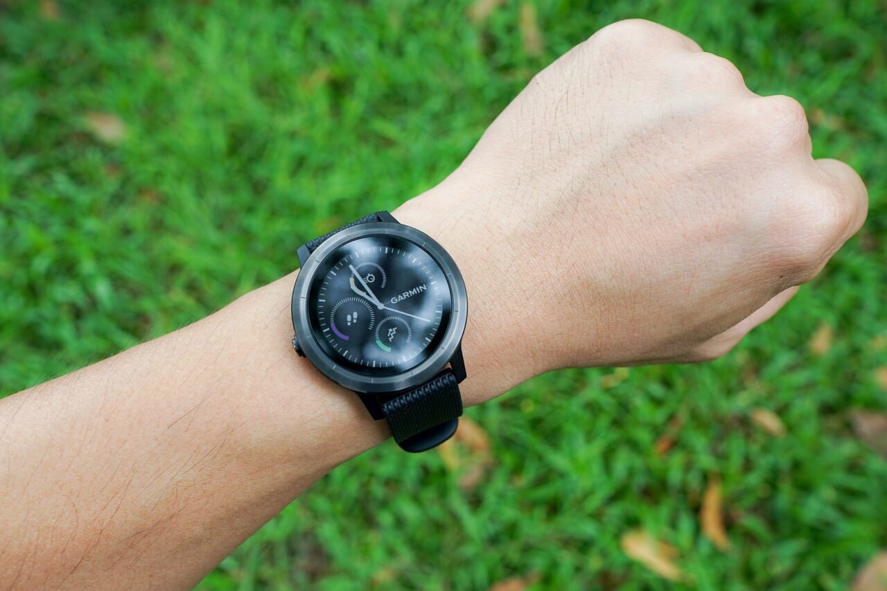 Zdjęcie to tekstu jaki smartwatch do 500 zł kupić. Czarny smartwatch Garmin noszony na nadgarstku z zielonym tłem trawy.