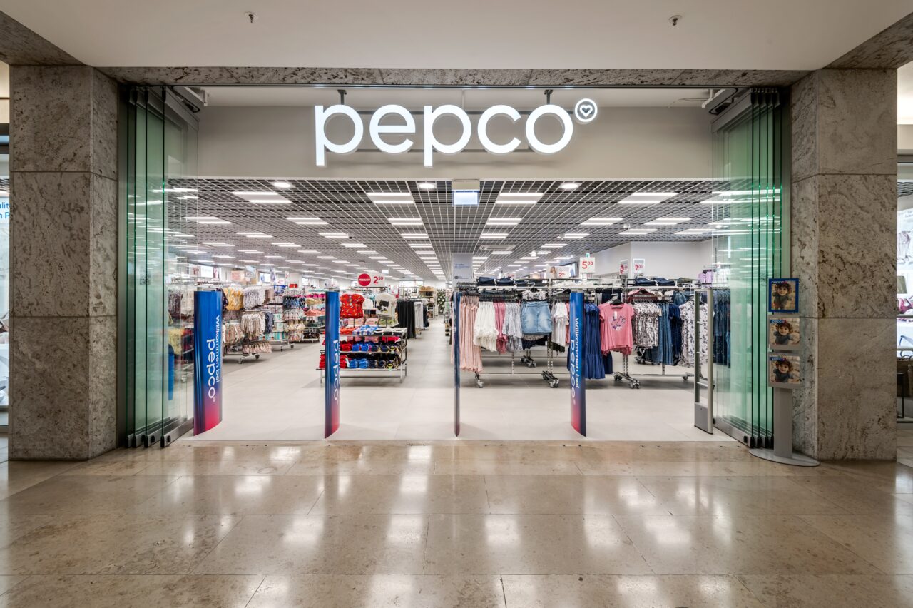 Wejście do sklepu Pepco, widoczne wewnętrzne wyposażenie i odzież na wieszakach.