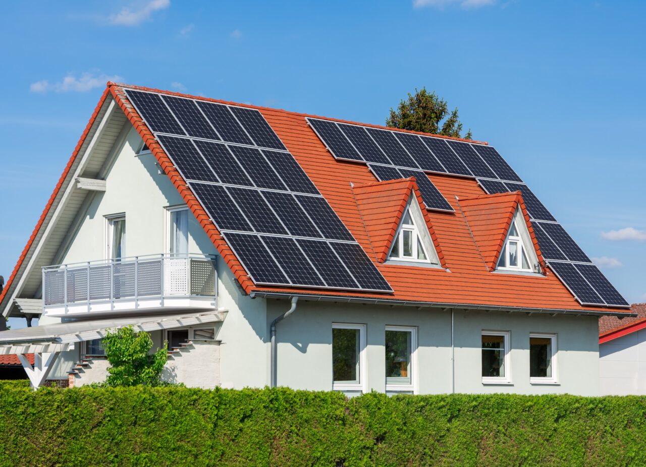 Fotowoltaika. Dom jednorodzinny z czerwonym dachem i instalacją paneli słonecznych na dachu.