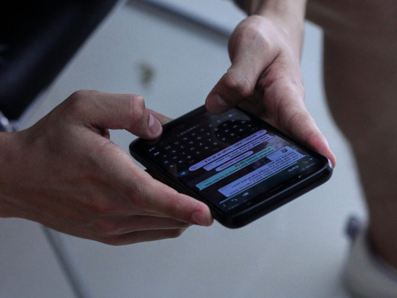 Osoba trzymająca i przeglądająca smartfon z klawiaturą QWERTY i otwartym ekranem czatu.