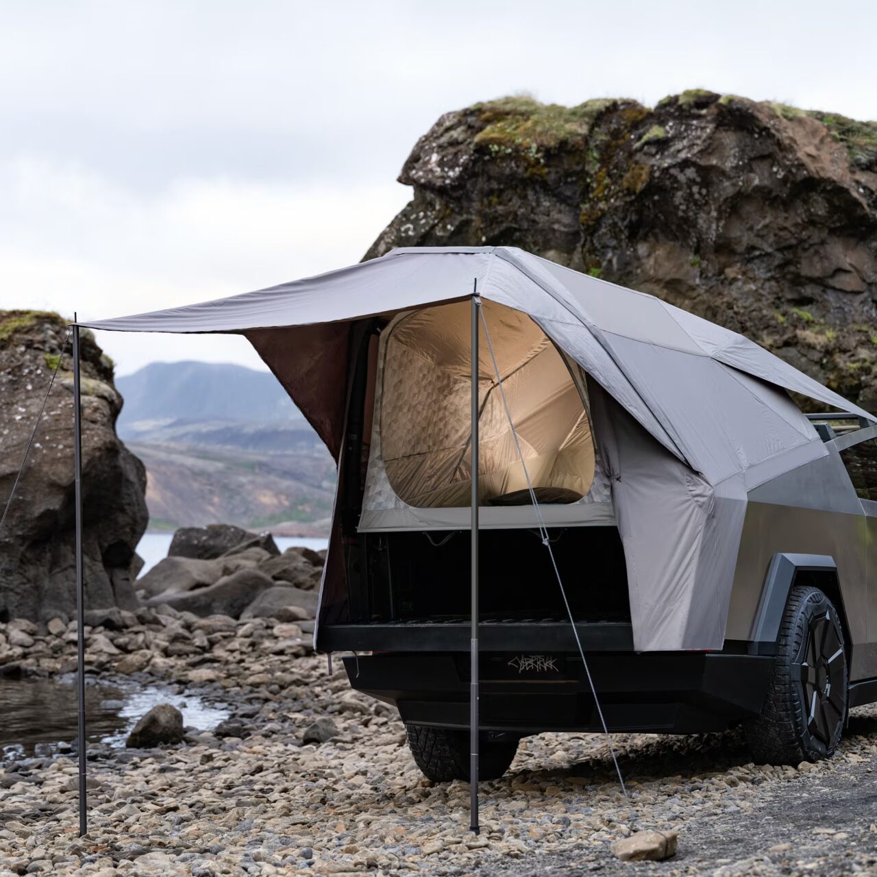 Namiot dachowy zamontowany na pickupie, zaparkowanym wśród kamieni przy strumieniu, z widokiem na górzysty krajobraz.