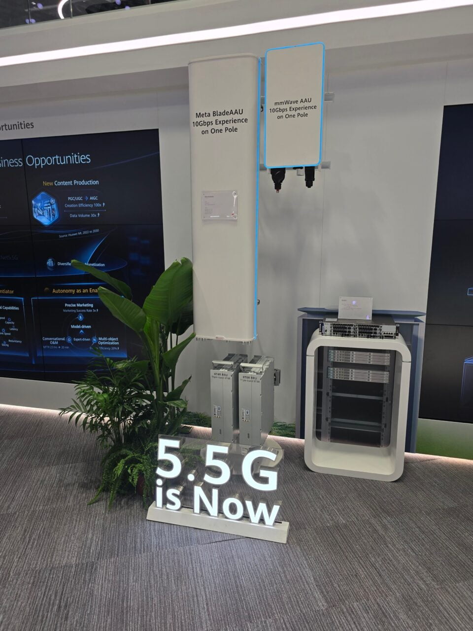 Stoisko Huawei 5.5G na targach MWC 2024 z urządzeniami technologicznymi, w tym urządzenia sieciowe typu AAU, napis "5.5G is NOW" na podłodze oraz reklama "Meta BladeAAU 10Gbps Experience on One Pole". Obok znajduje się mała zielona roślinność.