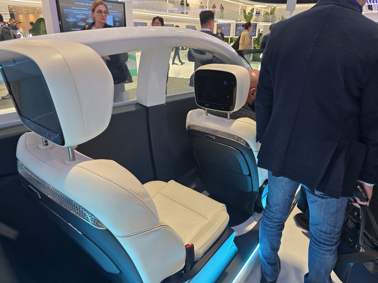 Stoisko Huawei 5.5G na targach MWC 2024. Wnętrze futurystycznego pojazdu z białymi fotelami i zaawansowanymi wyświetlaczami, otoczone ludźmi oglądającymi ekspozycję.