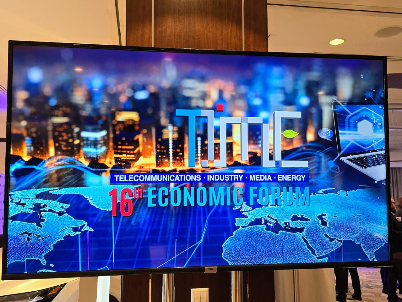 Ekran prezentacyjny 16. Forum Ekonomicznego Time (FG Time) z grafiką przedstawiającą zarysy mapy świata oraz symbole telekomunikacji, przemysłu, mediów i energii na tle rozmytego zdjęcia nocnego miasta.
