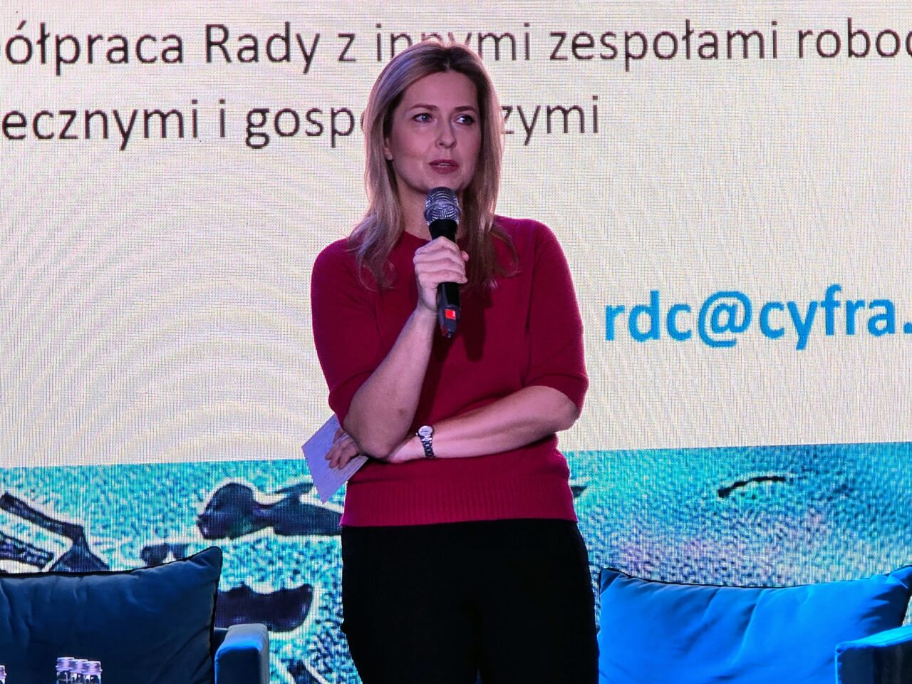 Przewodnicząca Rady ds. Cyfryzacji Agnieszka Jankowska podczas 16. FG Time. Kobieta stojąca na scenie trzyma mikrofon i prezentuje się przed wielkim ekranem z projekcją tekstu.