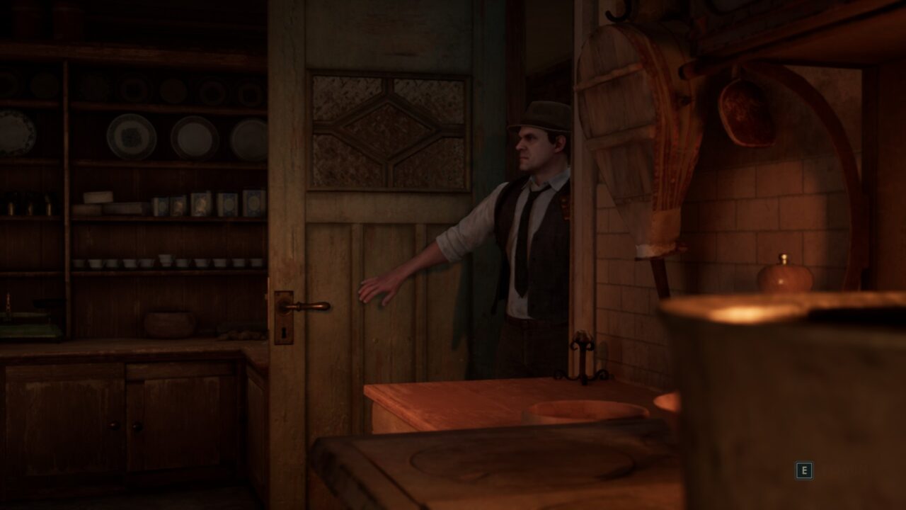 Mężczyzna w kapeluszu i kamizelce stojący w staroświeckiej kuchni, oparty o framugę drzwi.