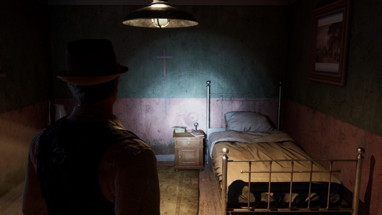 Mężczyzna w kapeluszu stoi tyłem do kamery w ciemnym, surowo urządzonym pokoju z metalowym łóżkiem, drewnianą szafką nocną i obrazem na ścianie, powyżej którego znajduje się krzyż.