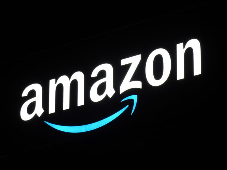 Podświetlony znak firmowy "Amazon" z białymi literami na czarnym tle i charakterystycznym niebieskim strzałkowym uśmiechem pod napisem.