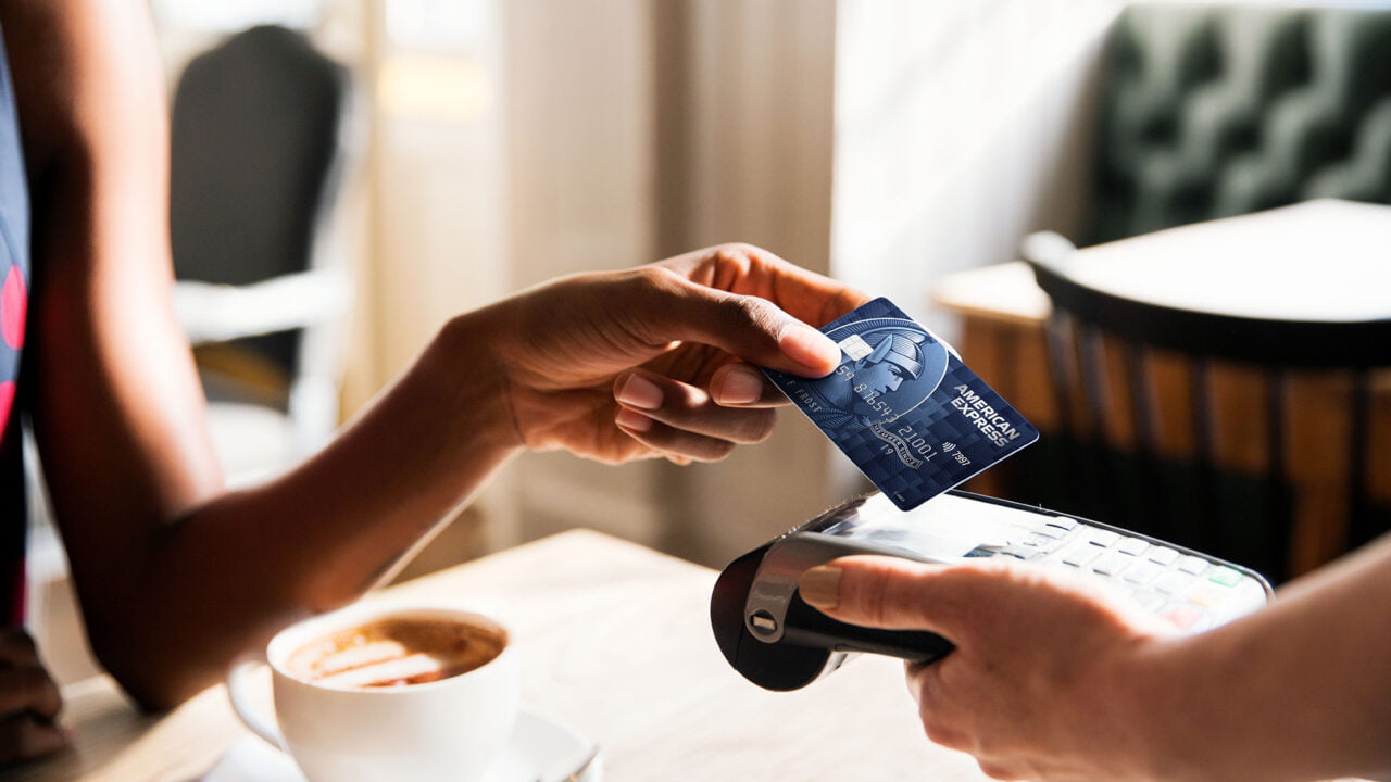 Osoba płaci kartą kredytową przy użyciu terminala płatniczego, w tle filiżanka z kawą na stole w kawiarni. Wyciek danych kart kredytowych american express