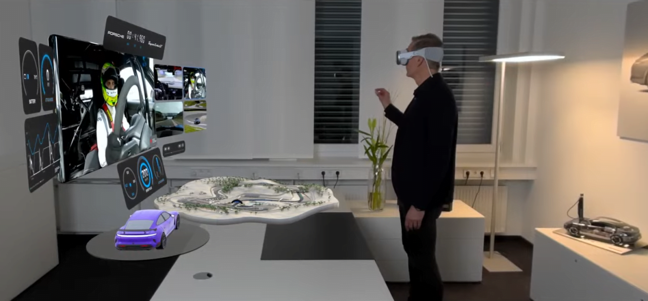 Mężczyzna w okularach VR stoi w nowoczesnym pokoju i patrzy na wirtualne ekrany z danymi wyścigowymi oraz model samochodu sportowego, a w tle widoczne są modele pojazdów i miniaturowy tor wyścigowy.