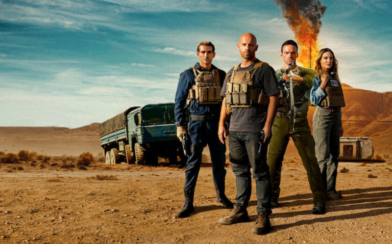 Kadr z filmu Cena strachu od Netflix. Czterech uzbrojonych ludzi w taktycznym ubiorze stojących na pustyni z płonącą wieżą wiertniczą w tle.