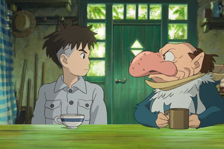 Kadr z filmu Chłopiec i czapla. Postać anime z brązowymi włosami i w szarej koszuli siedzi naprzeciwko kreskówkowego charakterystycznego człowieka z dużym różowym nosem i w niebieskim ubraniu, obaj patrzą na siebie przy zielonym stole w drewnianym pomieszczeniu.