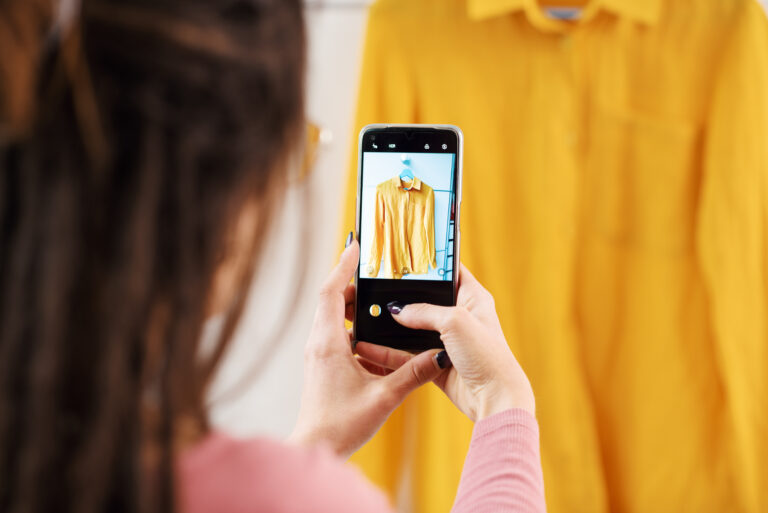 Osoba robi zdjęcie żółtej koszuli wiszącej na wieszaku za pomocą smartfona.