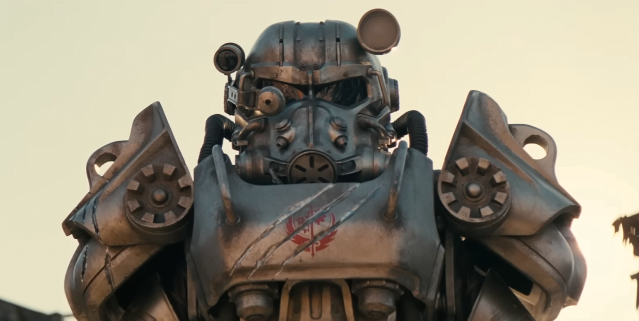 Serial Fallout na Amazon Prime. Zbliżenie na głowę i klatkę piersiową dużego robota w stylu post-apokaliptycznym z różnorodnymi metalowymi elementami i przetarciami, ze szczególnie widocznym czerwono-niebieskim emblematem na piersi.