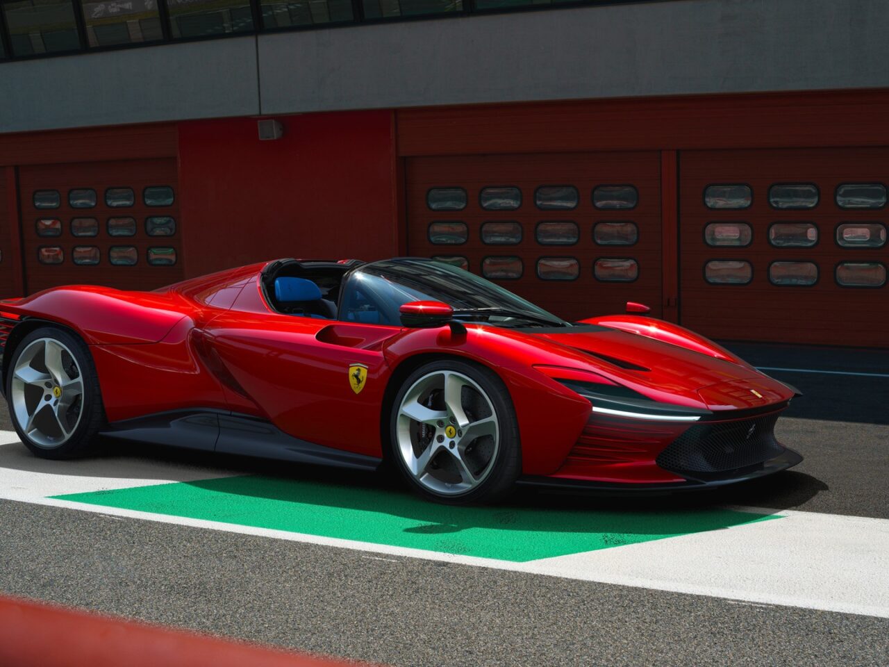 Elektryczne Ferrari. Czerwony samochód sportowy marki Ferrari zaparkowany na tle czerwonej ściany z przejściem dla pieszych w kolorach białym i zielonym.