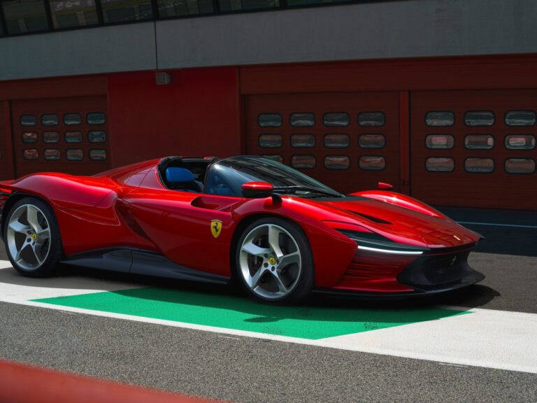 Czerwony samochód sportowy marki Ferrari zaparkowany na tle czerwonej ściany z przejściem dla pieszych w kolorach białym i zielonym.