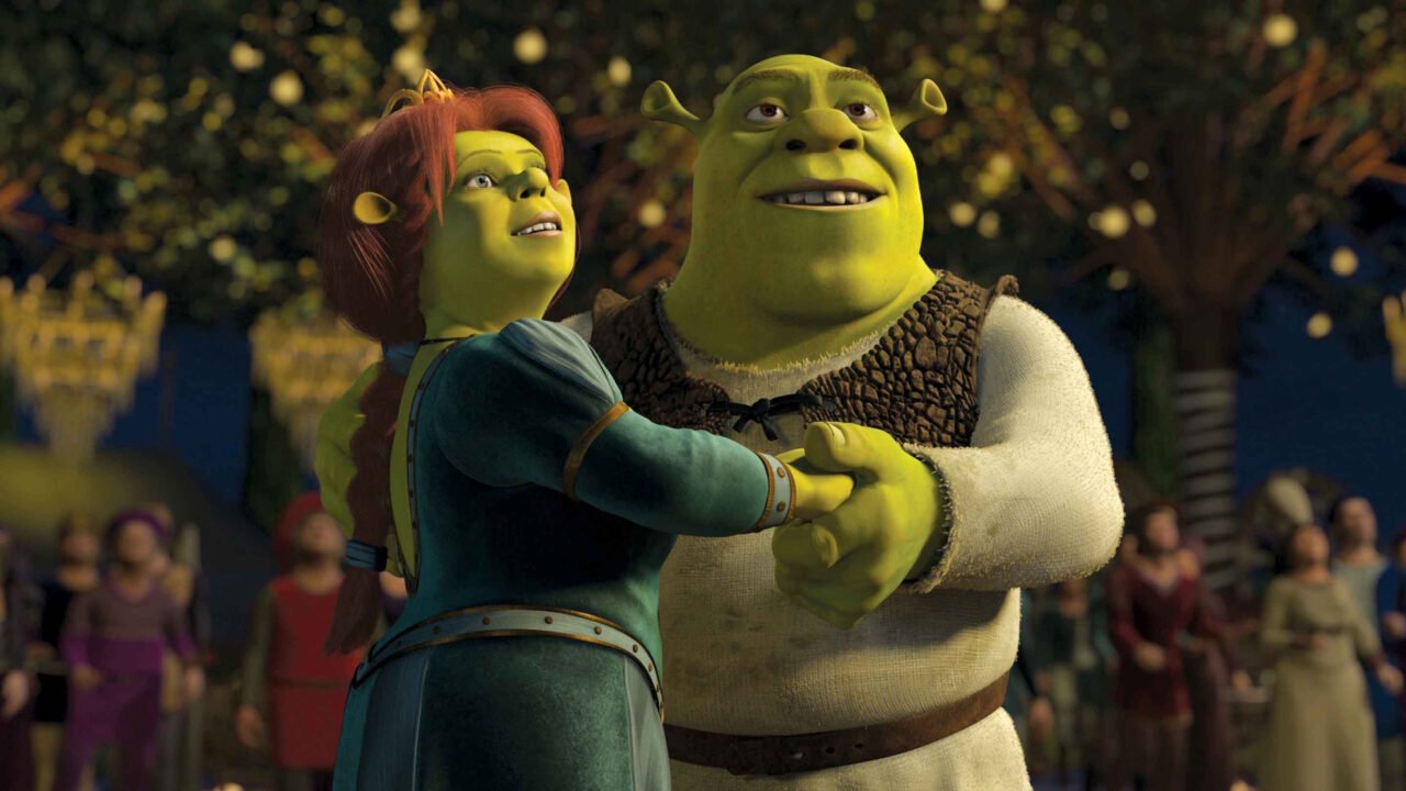 Animowane postacie z filmu Shrek, ogr i jego żona, tańczą razem, a w tle widoczni są ludzie przyglądający się im.