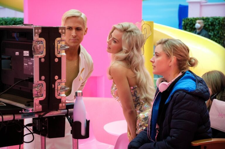 Trzy osoby, dwie kobiety i mężczyzna, przyglądają się z zaciekawieniem monitorowi na planie filmowym z jaskrawymi, różowymi i niebieskimi elementami scenografii.