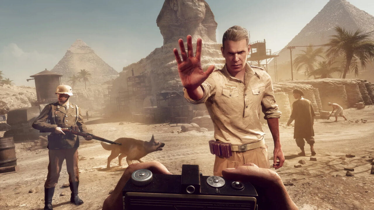 Kadr z gry Indiana Jones i Wielki krąg. Scena w grze wideo przedstawiająca mężczyznę w jasnej koszuli, który protestuje przeciwko robieniu zdjęcia, w tle widoczne są piramidy i Sfinks w Egipcie, a wokół poruszają się żołnierze oraz pies.
