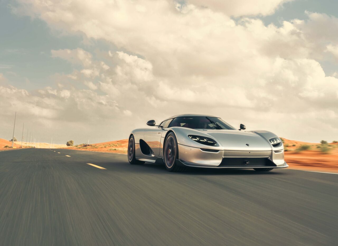 Srebrny samochód sportowy jedzie po asfaltowej drodze przez pustynny krajobraz.